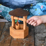 A child's hand winding up the bucket on the Ostheimer wooden wishing well toy. These wooden figures are part of a wide range of expertly hand crafted wooden toys here at Babipur. 