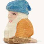 A Ostheimer wooden Xaver dwarf figure wearing a orange top and a blue hat on a cream background.