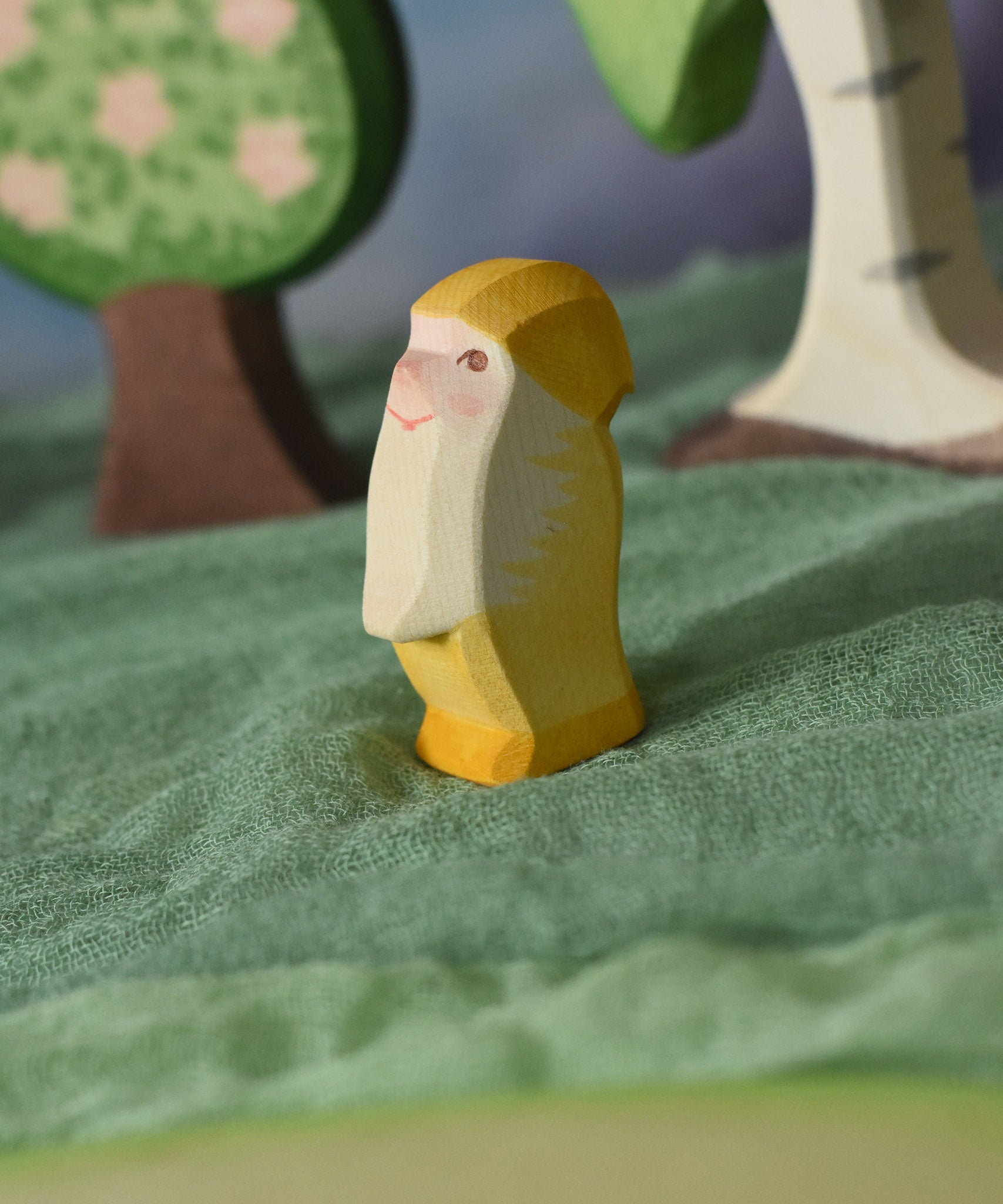 An Ostheimer yellow dwarf wooden toy figure placed in a small world play scene. The dwarf figure has a yellow coloured outfit with matching hat and a long white beard. The figure has been placed on a green coloured Ostheimer play scarf. This wooden figure is part of a large range of expertly hand crafted, Waldorf inspired, wooden toys here at Babipur. 