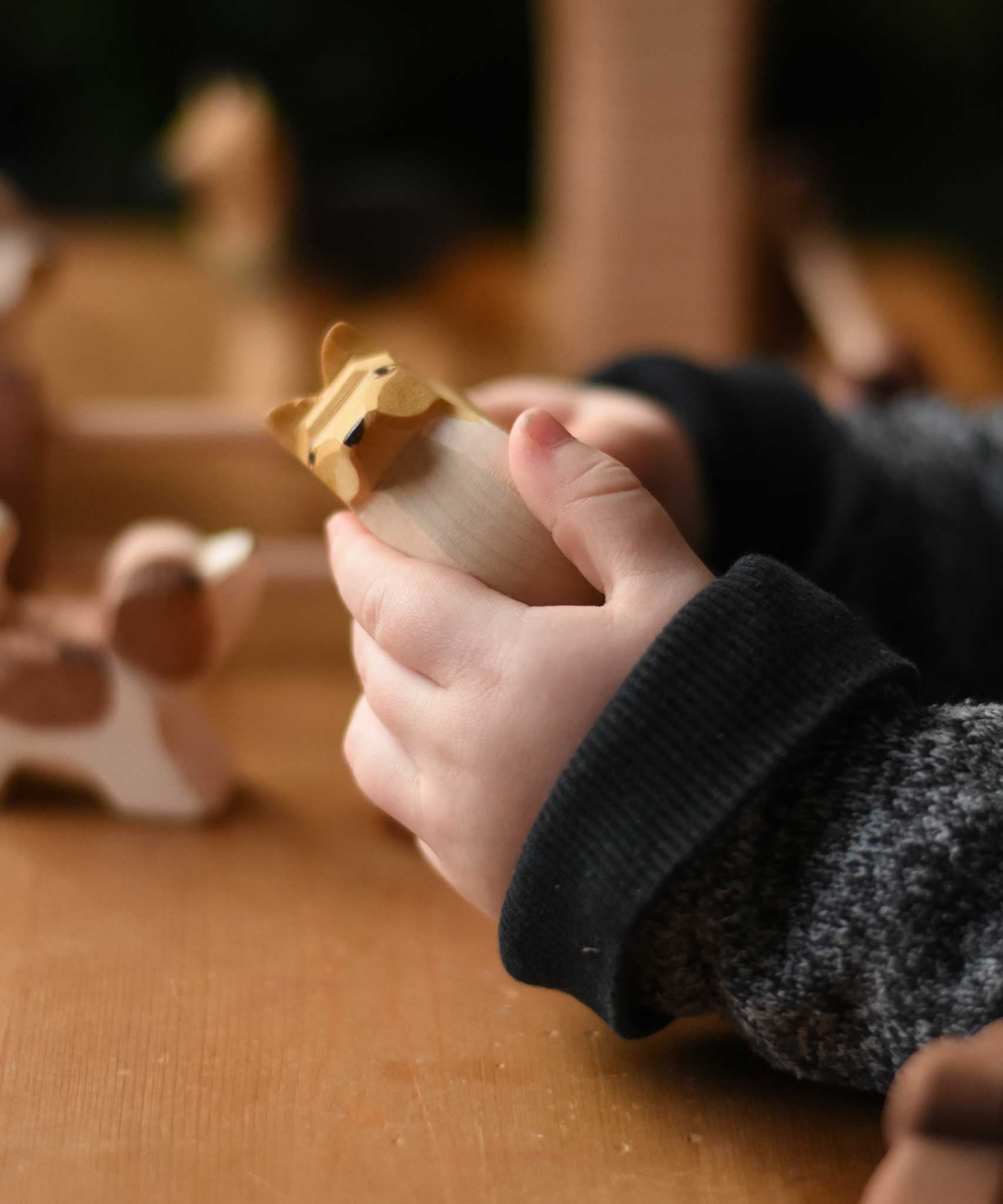 A close up of the Ostheimer collie dog's face wooden toy figure in a child's hand.  These wooden figures are part of a wide range of expertly hand crafted wooden toys here at Babipur. 