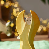 Ostheimer yellow guardian angel wooden toy figure placed on a green cotton cloth in a small world play scene. 