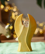 Ostheimer yellow guardian angel wooden toy figure placed on a green cotton cloth in a small world play scene. 