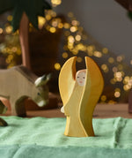 Ostheimer yellow guardian angel wooden toy figure placed on a green cotton cloth in a small world play scene. 