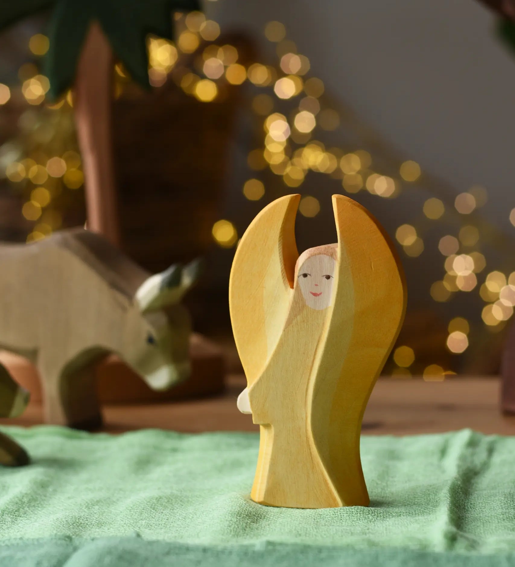 Ostheimer yellow guardian angel wooden toy figure placed on a green cotton cloth in a small world play scene. 