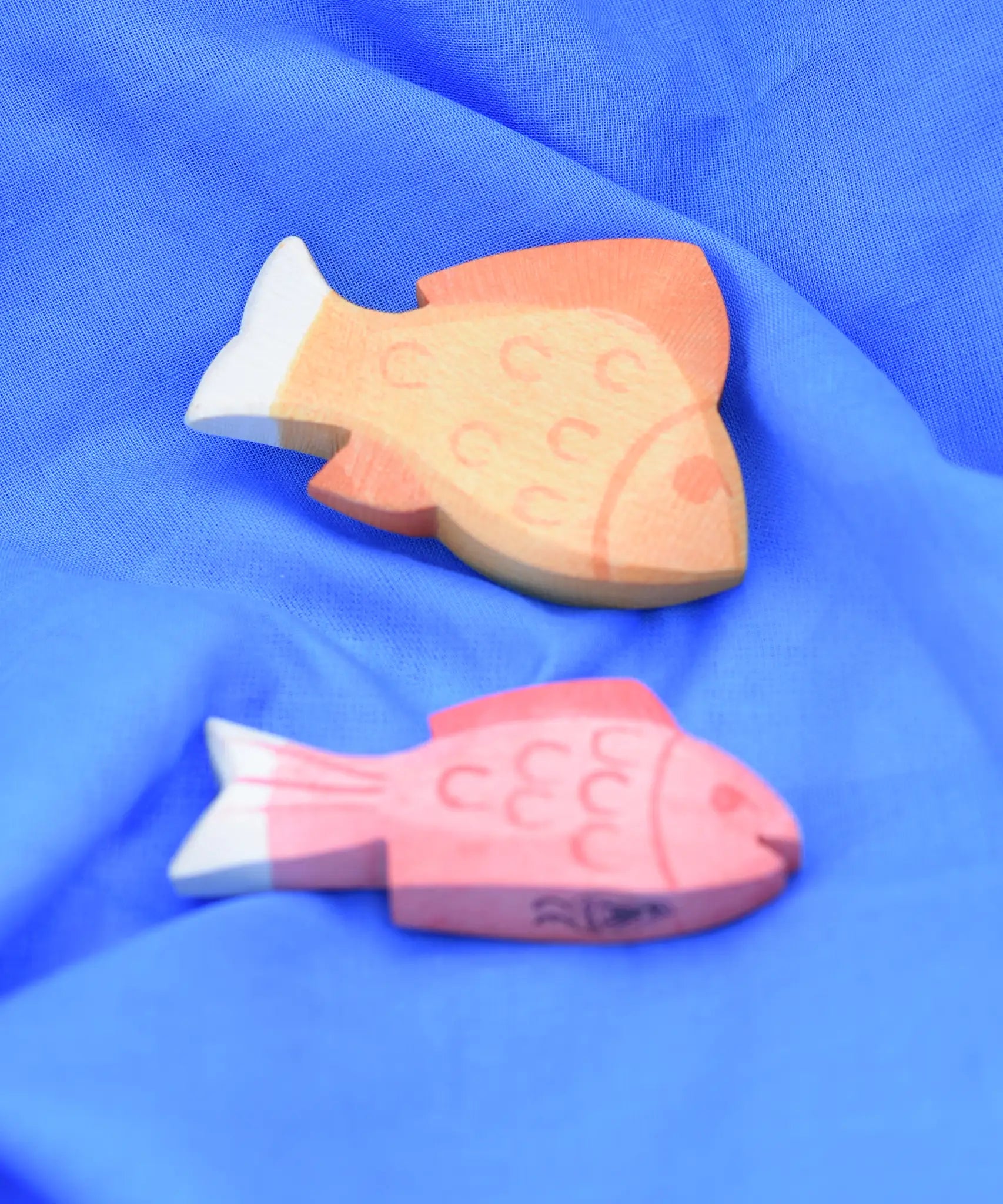Ostheimer yellow and red fish wooden toy figures placed on a  blue Laura's cotton play cloth.
