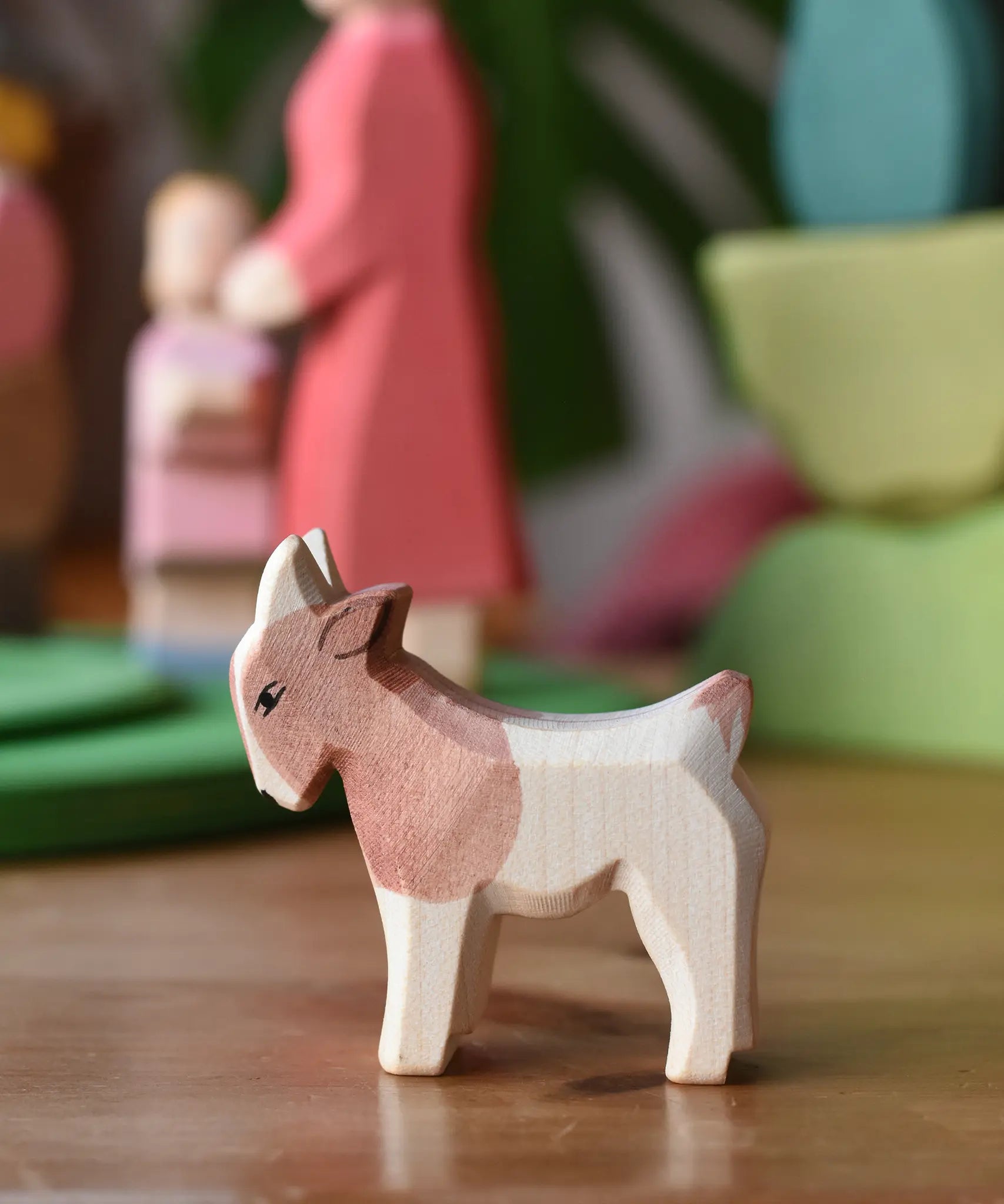 Ostheimer small standing brown and white goat wooden toy figure at the front of a play scene with other figures in the background. 