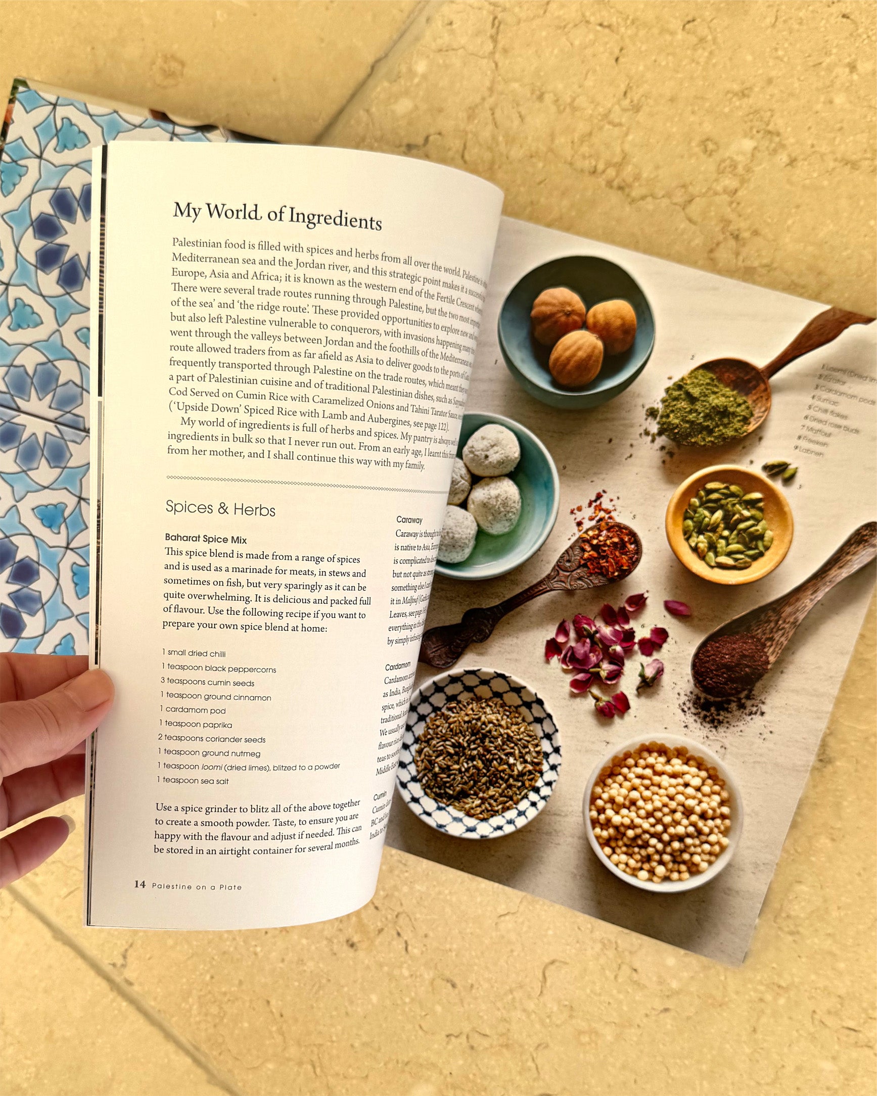 The cookbook 'Palestine on a Plate' is shown open to reveal a colourful page displaying spices and ingredients. 