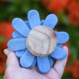 Back of a blue Papoose toys felt aster flower in an adult's hand showing the wooden disc base.