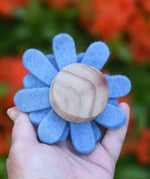 Back of a blue Papoose toys felt aster flower in an adult's hand showing the wooden disc base.