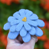 Blue Papoose toys felt aster flower in an adult's hand with orange azalea flowers in the background. 
