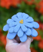 Blue Papoose toys felt aster flower in an adult's hand with orange azalea flowers in the background. 