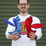 An adult standing outside holding the blue and red Papoose dragon side by side for size reference.