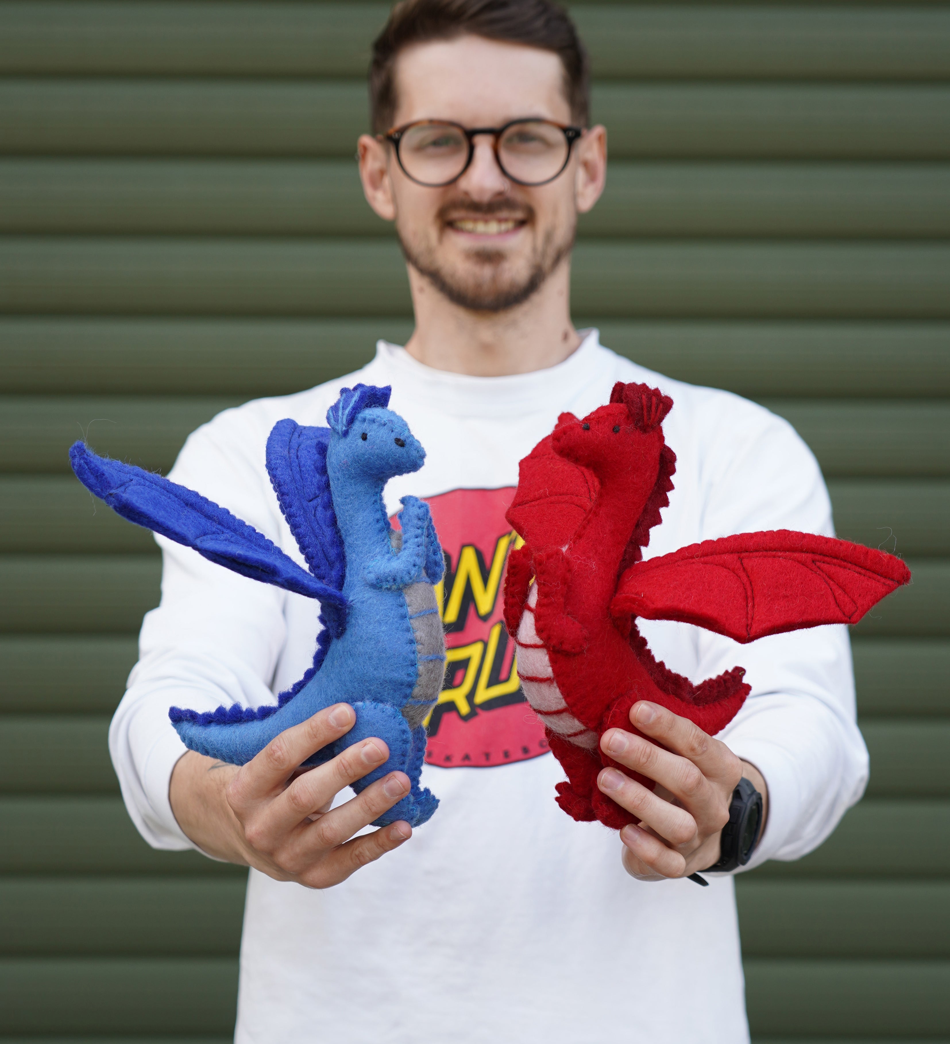 An adult standing outside holding the blue and red Papoose dragon side by side for size reference.