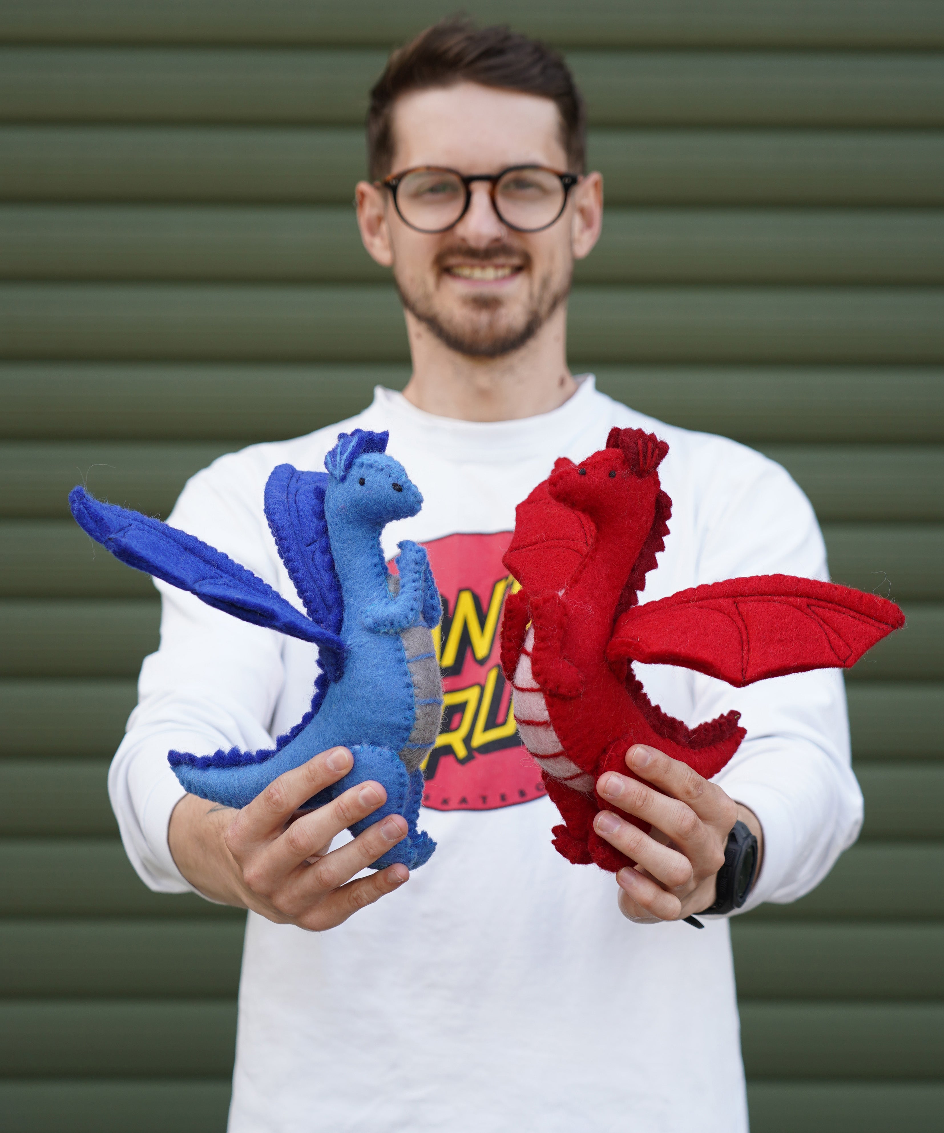 An adult standing outside holding the blue and red Papoose dragon side by side for size reference.