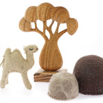 Papoose childrens felt camel toy on a white background next to a wooden African tree toy and some felt rocks