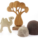 Papoose childrens felt camel toy on a white background next to a wooden African tree toy and some felt rocks