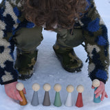 A child playing with the Papoose Toys Wooden Earth colours People peg dolls placed on a snow covered surface outoors.