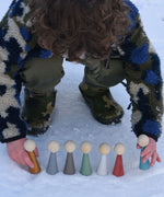 A child playing with the Papoose Toys Wooden Earth colours People peg dolls placed on a snow covered surface outoors.