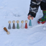 A child playing with the Papoose Toys Wooden Earth colours People peg dolls placed on a snow covered surface outoors.