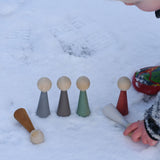 A child playing with the Papoose Toys Wooden Earth colours People peg dolls placed on a snow covered surface outoors.