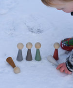 A child playing with the Papoose Toys Wooden Earth colours People peg dolls placed on a snow covered surface outoors.