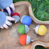Papoose Toys rainbow acorns placed in a wooden dish with a child's hands picking some up.