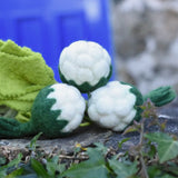 Papoose Toys felt cauliflower set of three placed on a stone wall outdoors. 