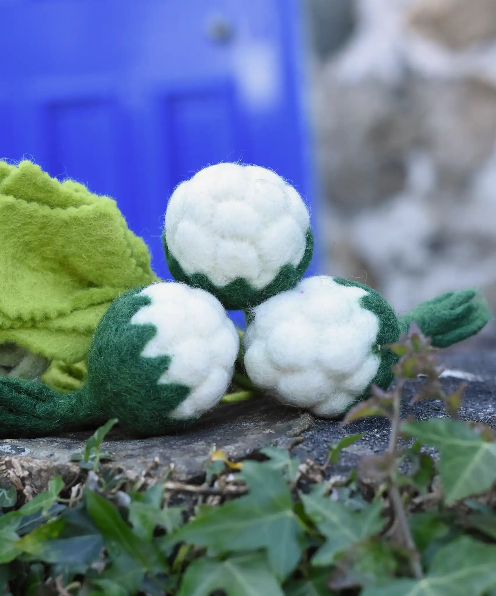Papoose Toys felt cauliflower set of three placed on a stone wall outdoors. 