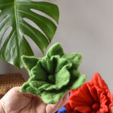 Green Papoose felted daffodil flower in an adult's hand with other colours seen in the background.