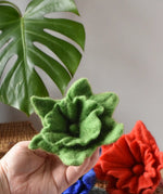 Green Papoose felted daffodil flower in an adult's hand with other colours seen in the background.