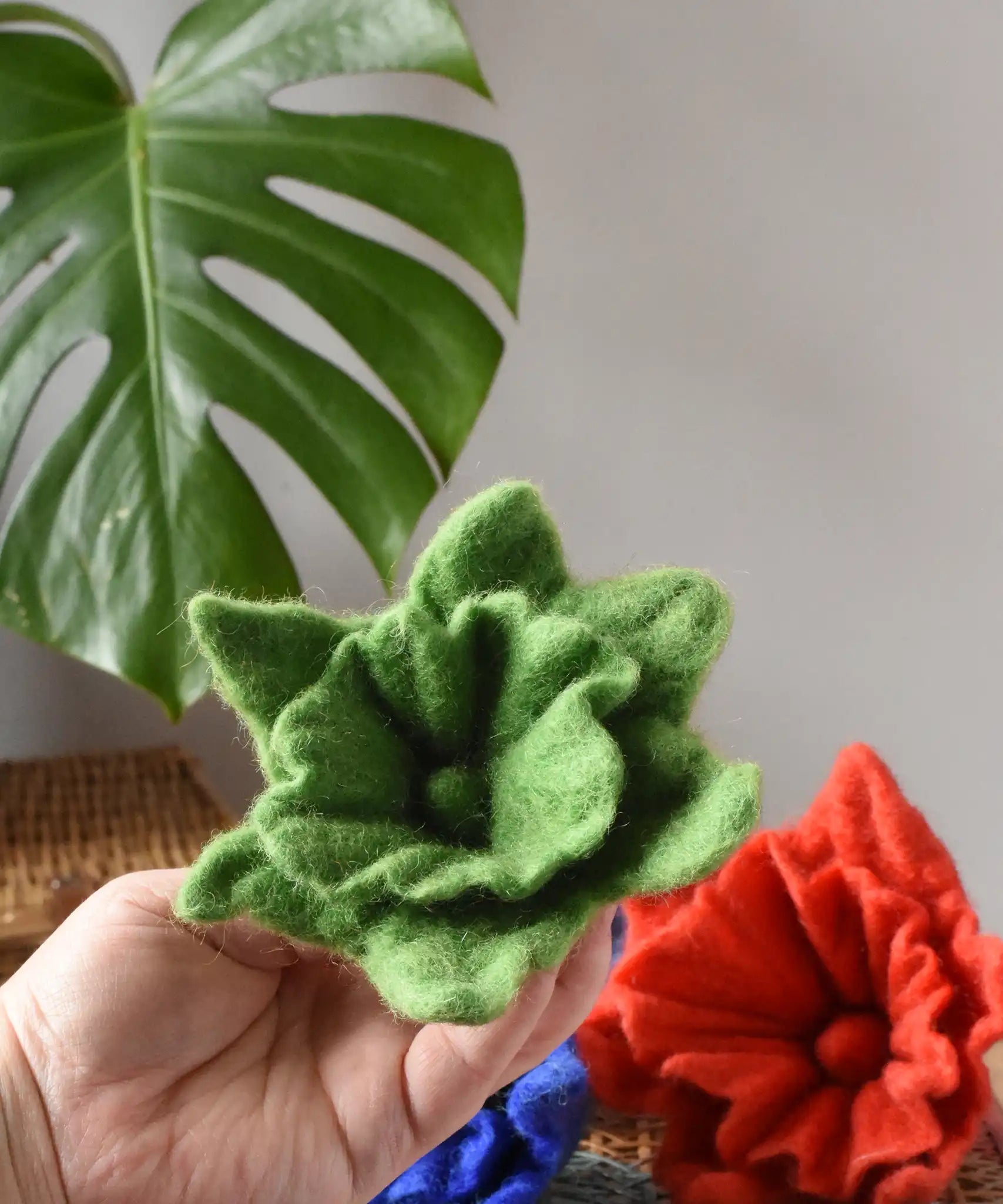 Green Papoose felted daffodil flower in an adult's hand with other colours seen in the background.