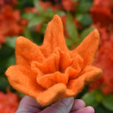 Orange Papoose felted daffodil flower in an adult's hand held up in front of orange azaela flowers. 