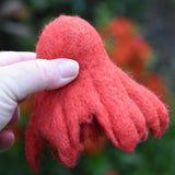 Papoose felted daffodil flower in red held upside down in an adult's hand. 