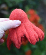 Papoose felted daffodil flower in red held upside down in an adult's hand. 