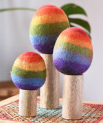 Papoose Toys felt rainbow trees in a set of three placed on a rattan top stool. 