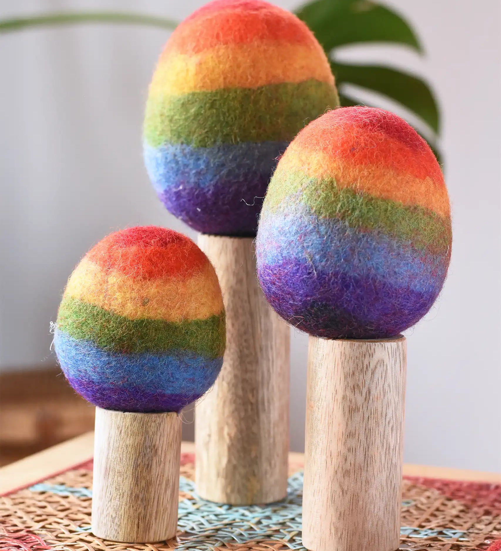 Papoose Toys felt rainbow trees in a set of three placed on a rattan top stool. 