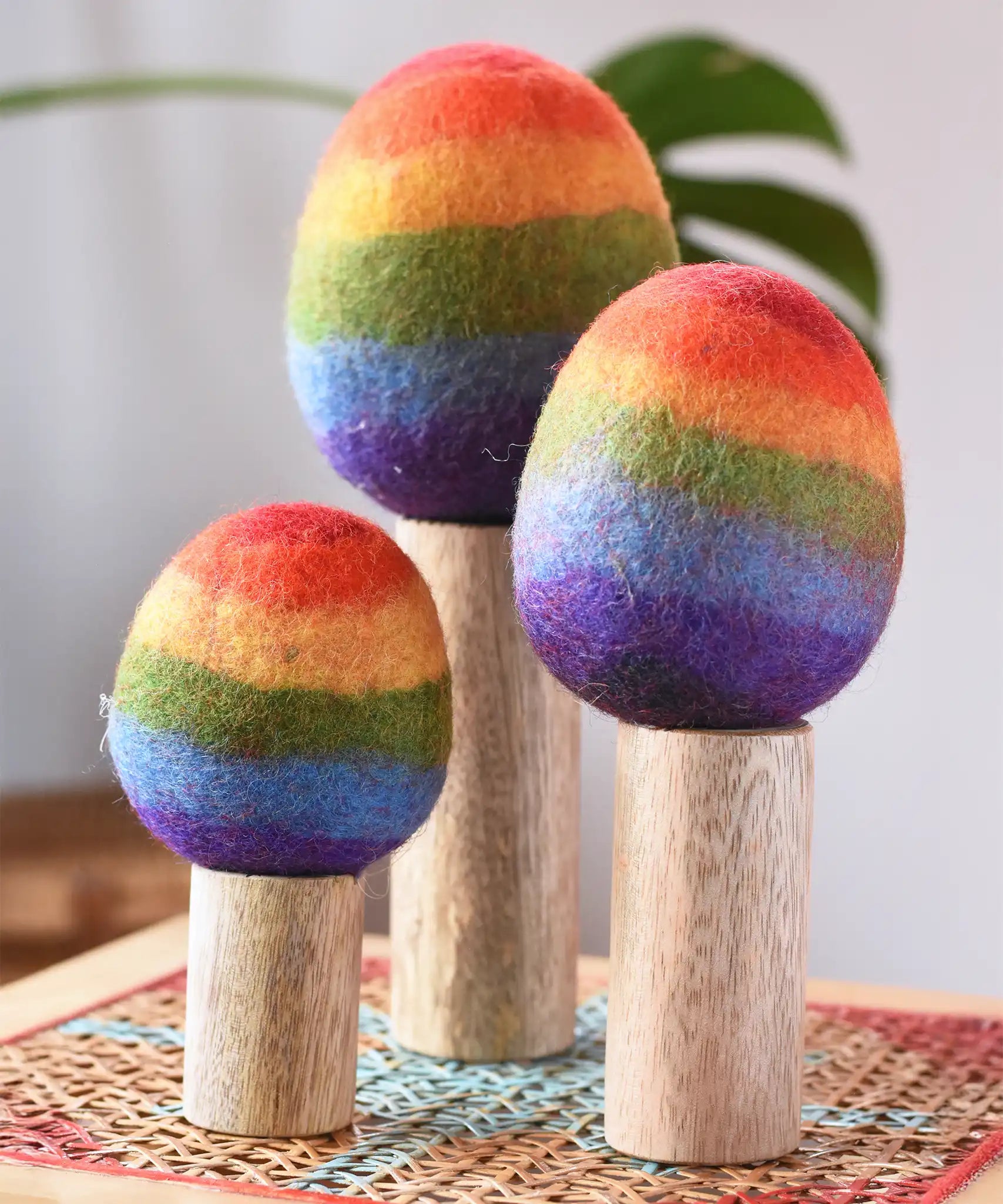 Papoose Toys felt rainbow trees in a set of three placed on a rattan top stool. 