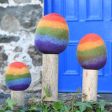 Papoose Toys felt rainbow trees in a set of three lined up on a stone wall outdoors. 