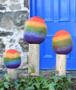 Papoose Toys felt rainbow trees in a set of three lined up on a stone wall outdoors. 