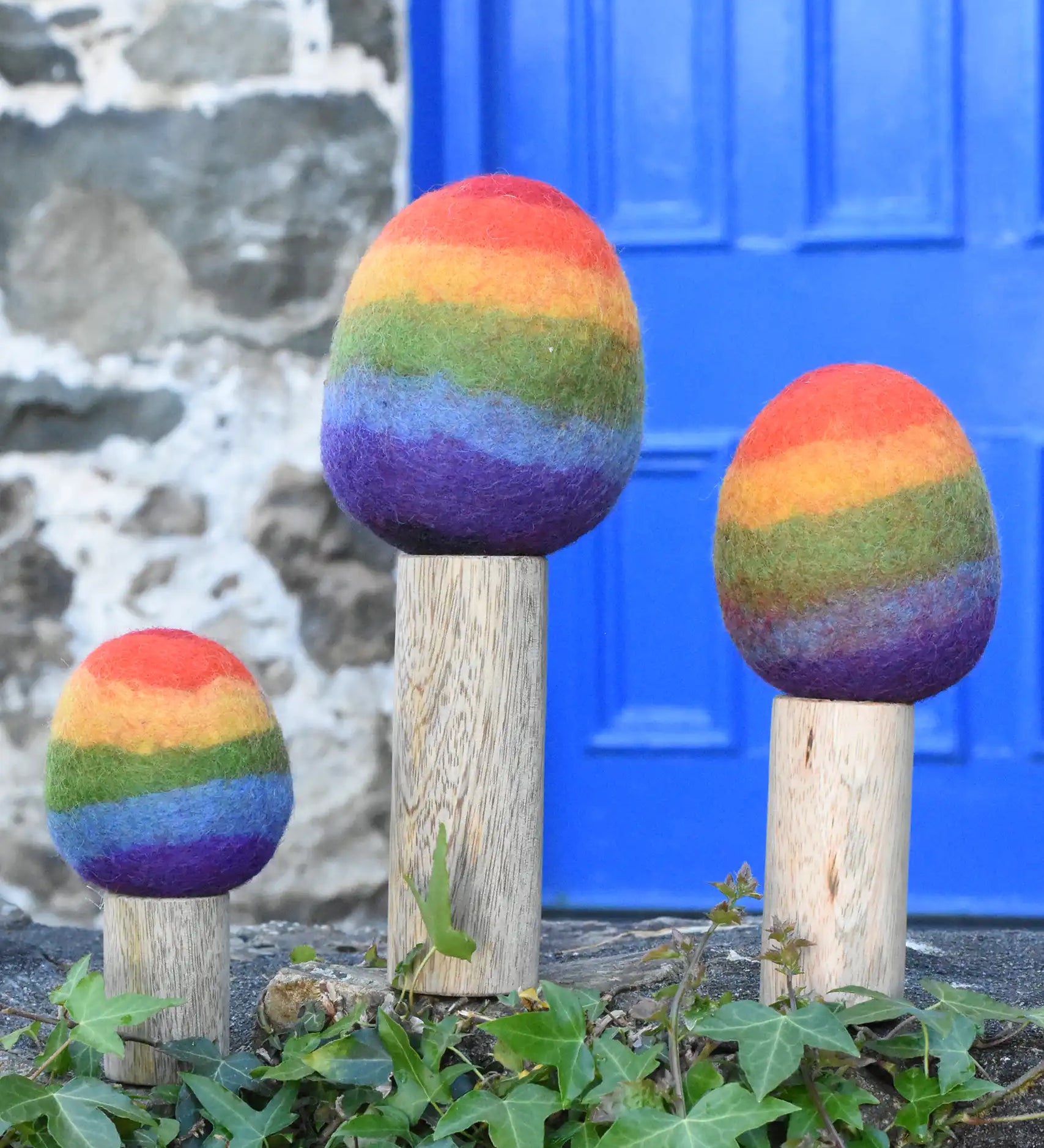 Papoose Toys felt rainbow trees in a set of three lined up on a stone wall outdoors. 