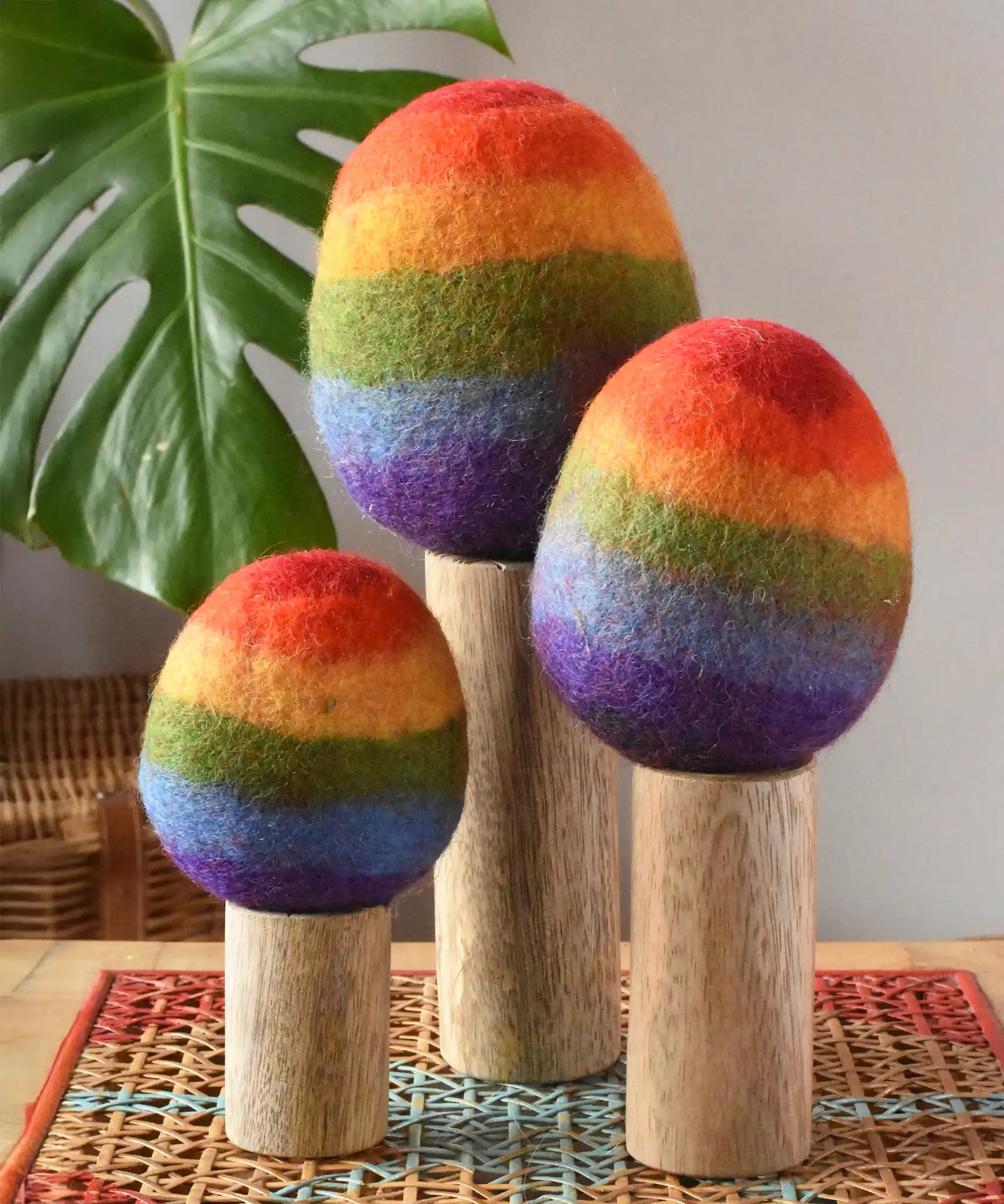 Papoose Toys felt rainbow trees in a set of three placed on a rattan top stool. 
