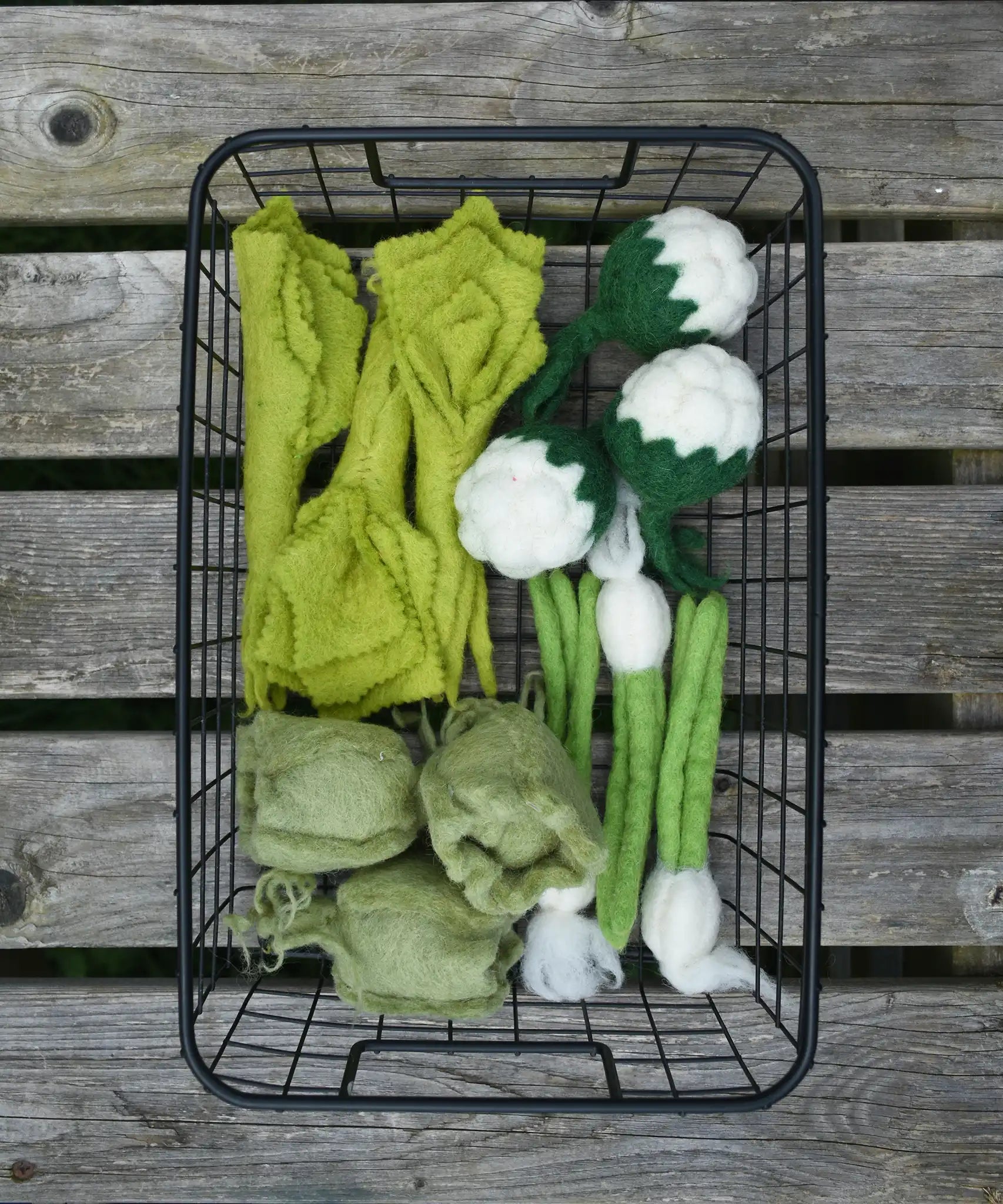 Papoose Toys felt vegetable play food placed in a black wire basket.