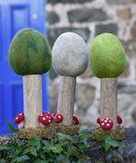 Papoose Toys Summer, Winter and Spring felt woodland trees lined up on a stone wall outdoors. placed on a rattan top stool. 