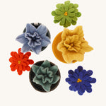 3 felted daffodils in coloured bowls with a blue, green and red aster laid next to them on a cream background