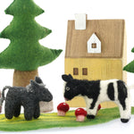 Close up of the Papoose soft felt donkey and cow toys on a Papoose play mat in front of a small wooden house