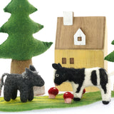 Close up of the Papoose soft felt donkey and cow toys on a Papoose play mat in front of a small wooden house
