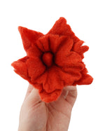 Close up of a hand holding a Papoose plastic-free soft felt flower toy on a white background