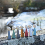 The Papoose Toys Wooden Earth colours People peg dolls placed on a stone surface outdoors.