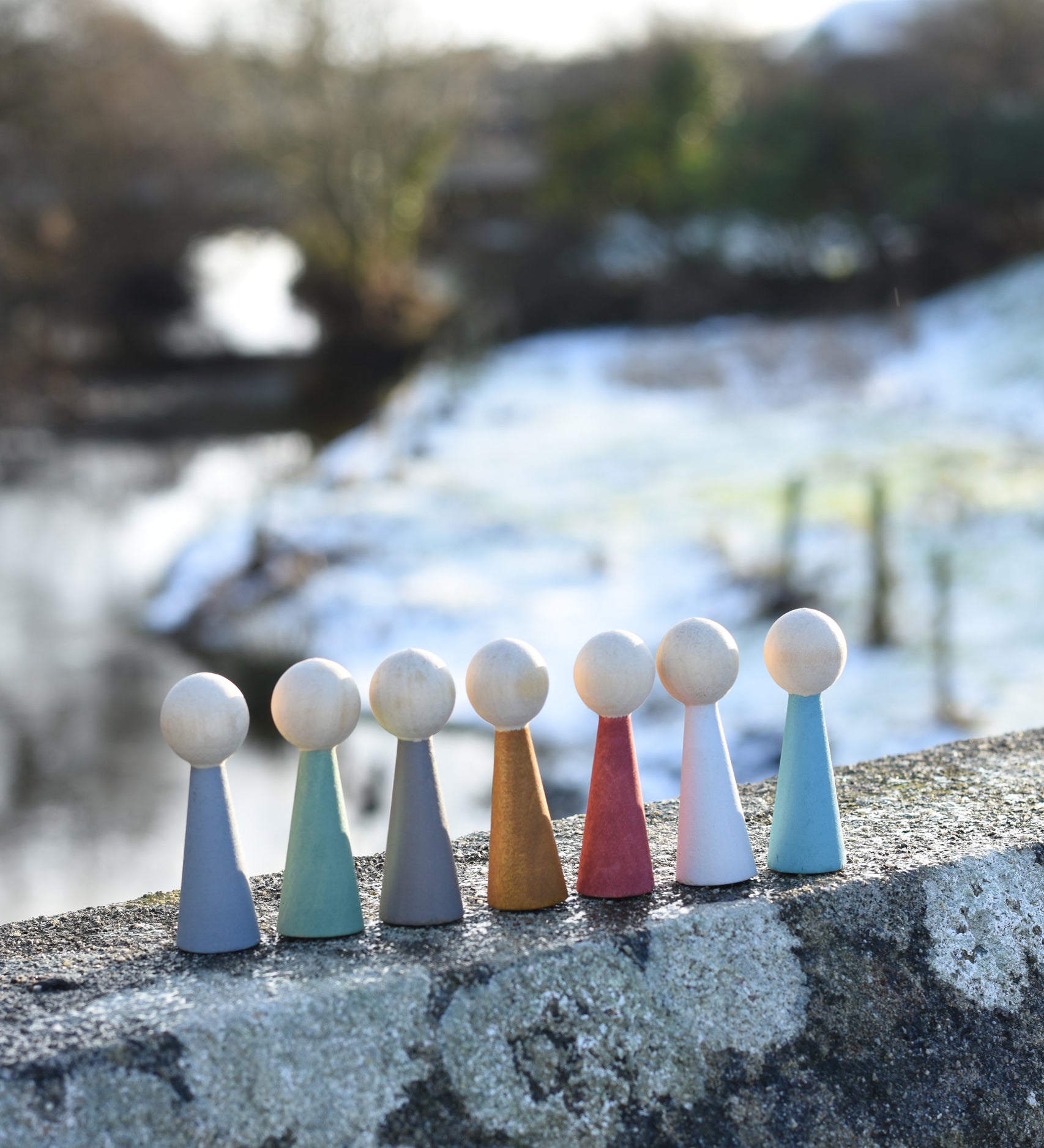 The Papoose Toys Wooden Earth colours People peg dolls placed on a stone surface outdoors.