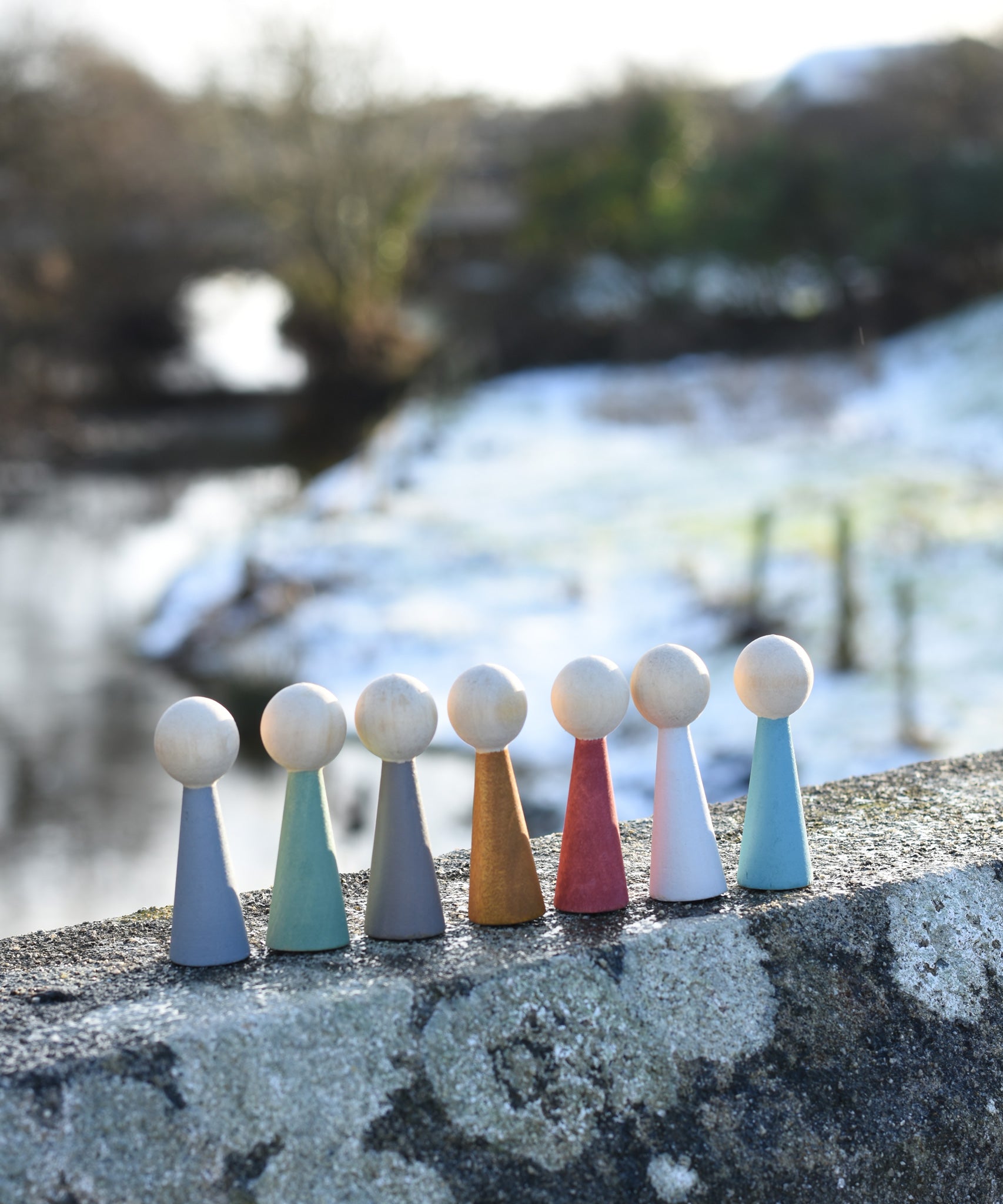 The Papoose Toys Wooden Earth colours People peg dolls placed on a stone surface outdoors.